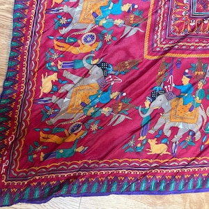 May include: A magenta silk scarf featuring a repeating pattern of grey elephants with orange and blue decorative saddles, riders in blue and orange tunics, and small yellow animals. The border has a green and purple leaf-like motif.