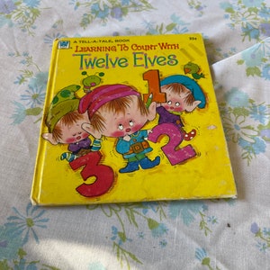 Peut inclure: Un livre pour enfants vintage intitulé "Learning to Count with Twelve Elves". La couverture est jaune et présente des illustrations d'elfes et les chiffres 1, 2 et 3. Le livre est un livre "Tell-a-Tale".