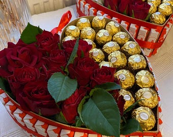 May include: Two heart-shaped boxes filled with red roses and gold-wrapped chocolates. The boxes are made of red and white cardboard and are decorated with red ribbon.