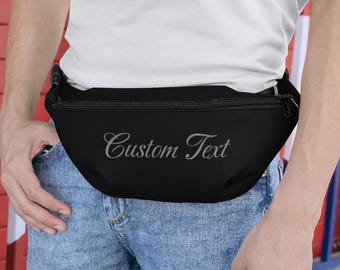 Op de afbeelding: Een zwarte heuptas met een ritssluiting en de tekst "Custom Text" geborduurd in zilver aan de voorkant.