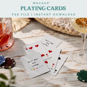 May include: A mockup image of playing cards with the text "MOCKUP PLAYING CARDS PSD FILE | INSTANT DOWNLOAD". The cards are white with red hearts and black spades. A glass of cocktail and poker chips are also visible.