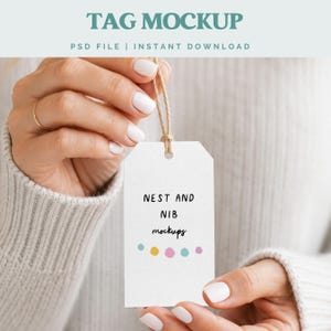 Pode incluir: Uma maquete de etiqueta branca com o texto "TAG MOCKUP" no topo e "PSD FILE | INSTANT DOWNLOAD" abaixo. A etiqueta tem as palavras "NEST AND NIB mockups" e pontos coloridos. A etiqueta é segurada por uma pessoa.