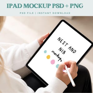 May include: An iPad mockup with the text "NEST AND NIB mockup" on the screen. The image shows a person holding the tablet and using a stylus. The top of the image has the text "IPAD MOCKUP PSD + PNG".