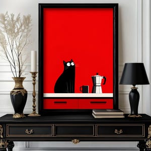 Puede incluir: Una lámina artística enmarcada con un fondo rojo brillante y sólido, que muestra un gato negro sentado sobre una encimera blanca junto a una taza negra y una cafetera italiana plateada. Debajo, se ven dos cajones rojos con tiradores negros.
