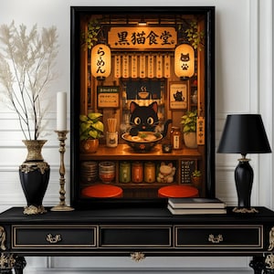 Könnte beinhalten: Ein gerahmter Kunstdruck, der das Innere eines gemütlichen japanischen Ramen-Ladens mit einer schwarzen Katze beim Nudelessen zeigt. Die Szene bietet warmes Licht, hängende Laternen mit japanischem Text, Holztresen und verschiedene Küchengläser.