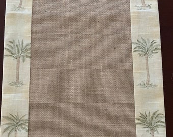 May include: A rectangular table runner with a natural burlap center and a patterned border. The border features a repeating design of palm trees in shades of green and brown against a cream-colored background. The runner is designed for home decor.