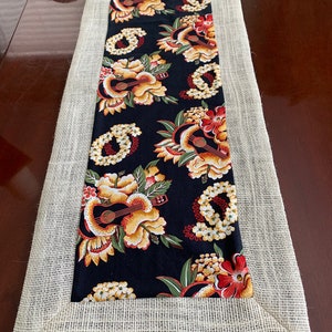 May include: A black and white table runner with a floral and ukulele pattern. The runner has a burlap border.
