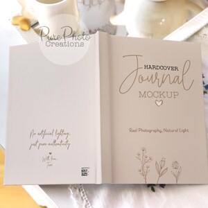 May include: A white hardcover journal mockup with the text "HARDCOVER Journal MOCKUP" in brown script font. The back cover has the text "No artificial lighting, just pure authenticity. With love, Tam" in brown text. The journal is on a white surface with a floral pattern.