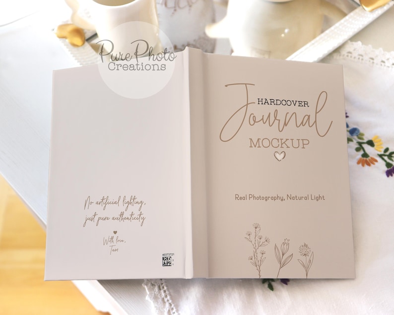 May include: A white hardcover journal mockup with the text "HARDCOVER Journal MOCKUP" in brown script font. The back cover has the text "No artificial lighting, just pure authenticity. With love, Tam" in brown text. The journal is on a white surface with a floral pattern.