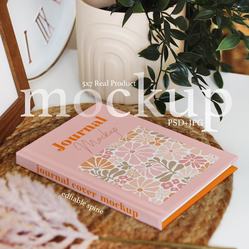 Pode incluir: Uma maquete de di&aacute;rio rosa com um padr&atilde;o floral na capa. O di&aacute;rio tem uma lombada branca e uma borda laranja. O texto na capa diz "Journal Mockup" e "journal cover mockup" com as palavras "editable spine" abaixo. O di&aacute;rio est&aacute; sentado em um tapete tecido.