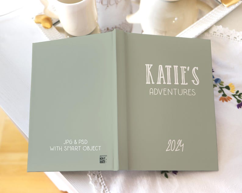 May include: A green journal with the text "KATIE'S ADVENTURES 2024" on the front cover. The back cover has the text "JPG & PSD WITH SMART OBJECT".