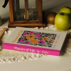Puede incluir: Un libro blanco con una encuadernaci&oacute;n rosa y un dise&ntilde;o floral en la portada. El t&iacute;tulo del libro es "Flavors of Life by Katie".