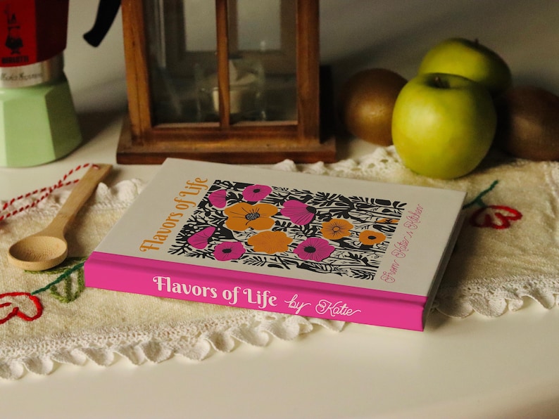 Puede incluir: Un libro blanco con una encuadernaci&oacute;n rosa y un dise&ntilde;o floral en la portada. El t&iacute;tulo del libro es "Flavors of Life by Katie".