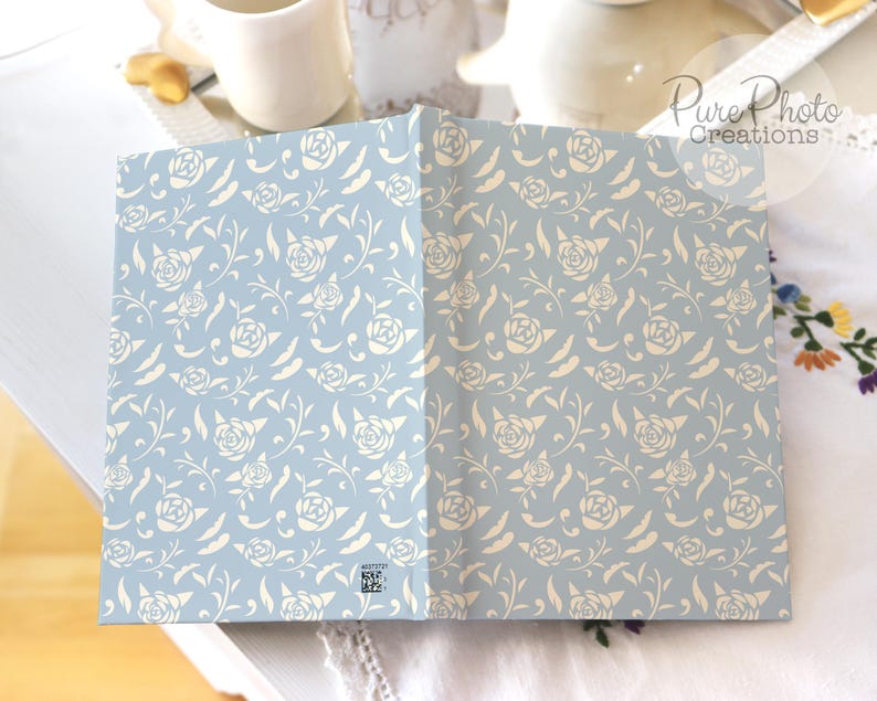 May include: A light blue notebook with a white floral pattern. The notebook is closed and lying flat on a white surface.