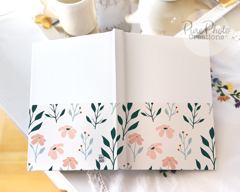 May include: A white journal with a floral design on the bottom edge. The design features pink flowers and green leaves on a white background.