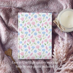 May include: A pink and blue floral patterned notebook on a fuzzy pink surface. The notebook is closed and has a white background with pink flowers and blue butterflies.