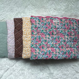 May include: Five rectangular quilted pouches with zippered closures, arranged in a row. The patterns include a green polka dot, a light pink floral, a dark brown micro-floral, a yellow floral, and a large pink and green rose floral print.