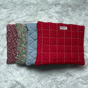 Peut inclure: Quatre pochettes rectangulaires matelassées disposées en rangée. De gauche à droite, les pochettes présentent un imprimé floral bordeaux foncé, vert, bleu clair et rouge avec une étiquette blanche portant l'inscription Satin & Sage.