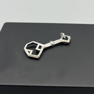 May include: A silver key pendant with a geometric design and the word "remarkable" inscribed on the shaft.