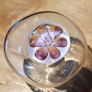 Peut inclure: Un bouchon de bouteille en verre transparent avec un motif de fleur violet et orange.