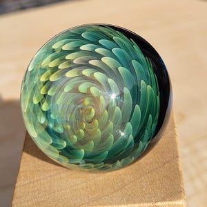 May include: A white ceramic mug with a black handle and the text "But First, Coffee" in a bold, black font. The mug is set against a blurred background, suggesting a cozy setting.