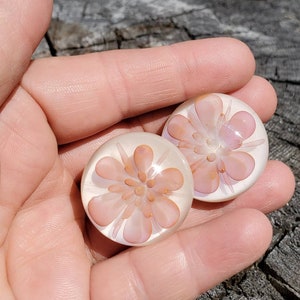 Puede incluir: Dos pisapapeles de vidrio rosa en forma de flor con fondo blanco y diseño de flor rosa claro.