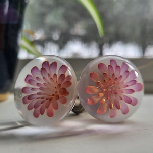 Puede incluir: Dos pomos redondos de vidrio transparente con diseños florales rosas y naranjas. Los pomos son brillantes.