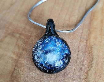 May include: A black glass pendant necklace with a blue and white galaxy design. The pendant is round and has a silver chain.