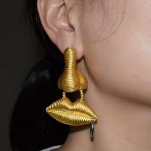 May include: Gold tone earrings with a lip design and a small ring charm. The earrings are made of twisted wire.