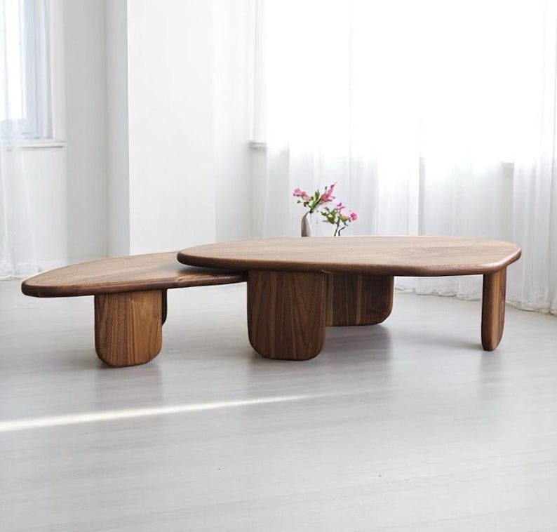 Op de afbeelding: Een houten salontafel met een unieke, organische vorm. De tafel bestaat uit twee delen, een groter ovaalvormig deel en een kleiner, rechthoekiger deel. De tafel is gemaakt van donker hout en heeft een natuurlijke afwerking.