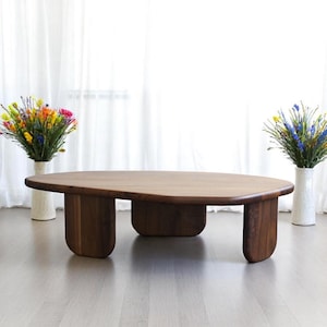 Op de afbeelding: Een grote, organisch gevormde salontafel van donker hout met vier unieke poten. De tafel staat op een lichtgrijze houten vloer.