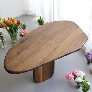 Op de afbeelding: Een unieke, organisch gevormde houten tafel met een donkerbruine afwerking. De tafel heeft een enkel, dik, afgerond poot die ook van hout is gemaakt.