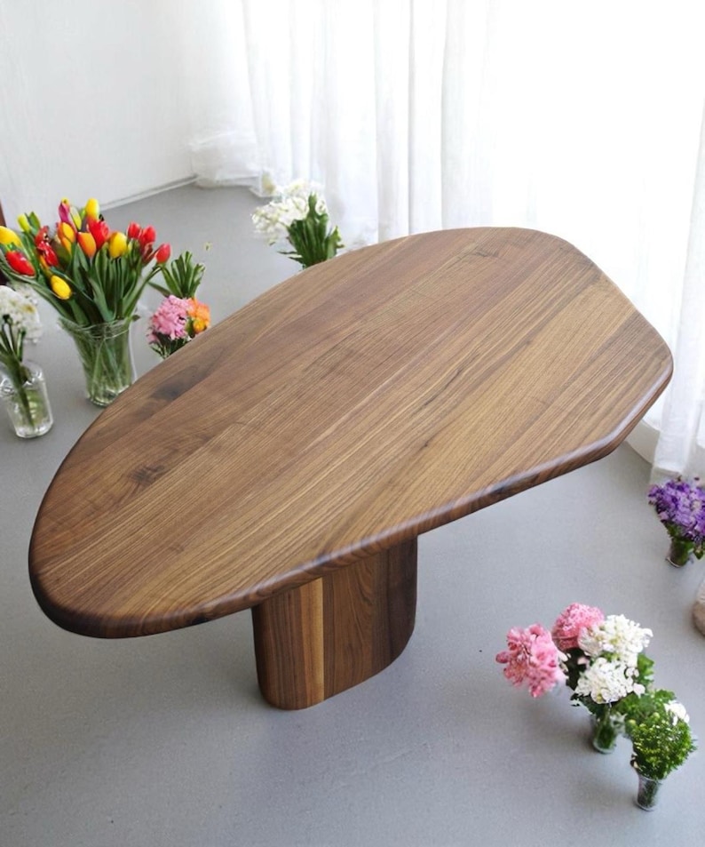 Op de afbeelding: Een unieke, organisch gevormde houten tafel met een donkerbruine afwerking. De tafel heeft een enkel, dik, afgerond poot die ook van hout is gemaakt.