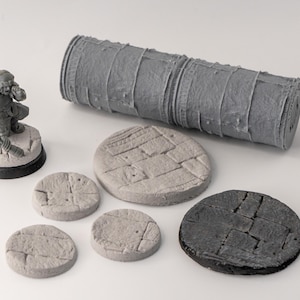 Peut inclure: Un ensemble de six bases rondes texturées pour figurines miniatures, comprenant un rouleau gris pour créer la texture. Les bases sont dans différentes nuances de gris et de noir.