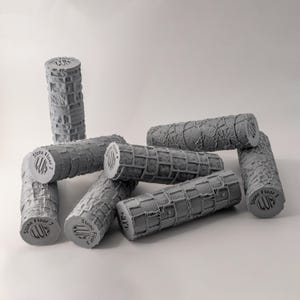 Op de afbeelding: Een verzameling grijze cilindrische rollers met een getextureerd oppervlak dat op stenen blokken lijkt. Elke roller heeft de tekst "Stone Floor" en een nummer. De rollers liggen op een witte ondergrond.