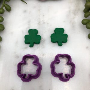May include: Two green shamrock-shaped cookie cutters and two purple shamrock-shaped cookie cutters.