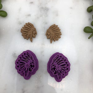 May include: Two pairs of Native American headdress cookie cutters. One pair is brown and the other pair is purple.