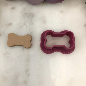 May include: A pink plastic dog bone cookie cutter and a brown clay dog bone.
