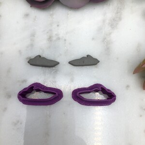 Può includere: Due tagliabiscotti in plastica viola a forma di motoscafo. I tagliabiscotti sono su una superficie bianca.