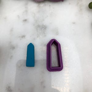 May include: Two cookie cutters, one purple and one blue, shaped like a pointed rectangle.