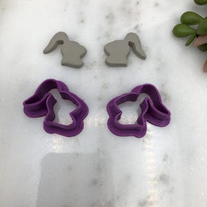 Könnte beinhalten: Zwei violette Plastik-Keksstempel in Form eines Hasen und zwei graue Tonhasenformen.