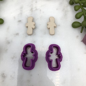 Può includere: Due tagliabiscotti in plastica viola a forma di croce con un motivo floreale. Due forme di croce in argilla beige con un motivo floreale.
