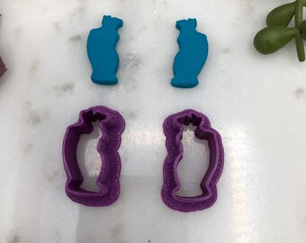 Può includere: Due stampini per biscotti a forma di bottiglia, uno blu turchese e l'altro viola. Gli stampini per biscotti sono su una superficie bianca.