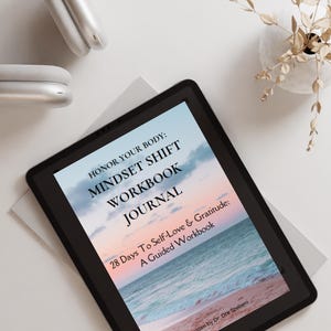 May include: A black tablet computer displaying the cover of a workbook titled "Honor Your Body: Mindset Shift Workbook Journal". The cover features a beach scene with a sunset sky and ocean waves. The text "28 Days To Self-Love & Gratitude: A Guided Workbook" is also visible on the cover. The book is written by Dr. Dre Szebeni.