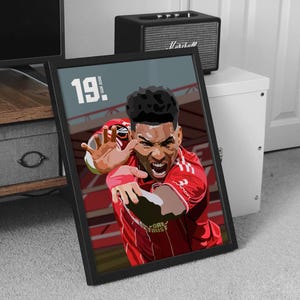 May include: Framed art print depicting a soccer player in a red jersey, in a dynamic pose. The player is reaching out with an intense expression. The number "19" is visible in the upper left corner. The background shows a stadium.