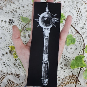 May include: A black and white illustration of a spiked mace on a black fabric patch. The mace has a round head with spikes and a long, cylindrical handle.