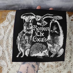 May include: Black iron-on patch with a white design of various animals including a fox, owl, rabbit, hedgehog, badger, and frog. The text "Respect The Locals" is written in a stylized font.