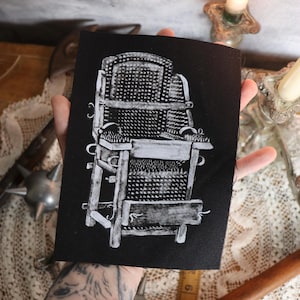 May include: A black and white illustration of a medieval torture device, a spiked chair, on a black fabric patch.