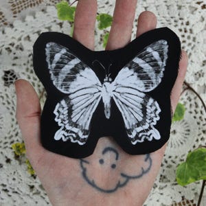 May include: Black fabric patch featuring a white butterfly design. The butterfly has black and white stripes on its wings.