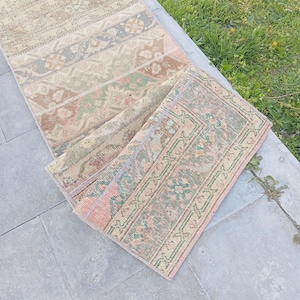 Pode incluir: Um tapete corredor vintage com um design de patchwork. O tapete apresenta uma mistura de cores suaves, incluindo bege, rosa, verde e azul. O tapete está parcialmente enrolado, mostrando seus intrincados padrões e texturas. O tapete está colocado sobre uma superfície de pedra.